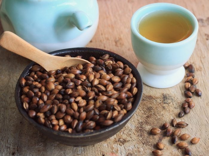 Un cuenco de cerámica con semillas de cebada tostadas con una tetera y una taza de té de cebada en una mesa de madera