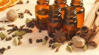 Bottles of cardamom essential oil and dried anise seeds, black peppercorns, cardamom, cinnamon sticks, nutmeg with sliced grapefruit on a wooden floor