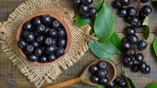 A wooden bowl and spoon of fresh chokeberries with leaves on a wooden table