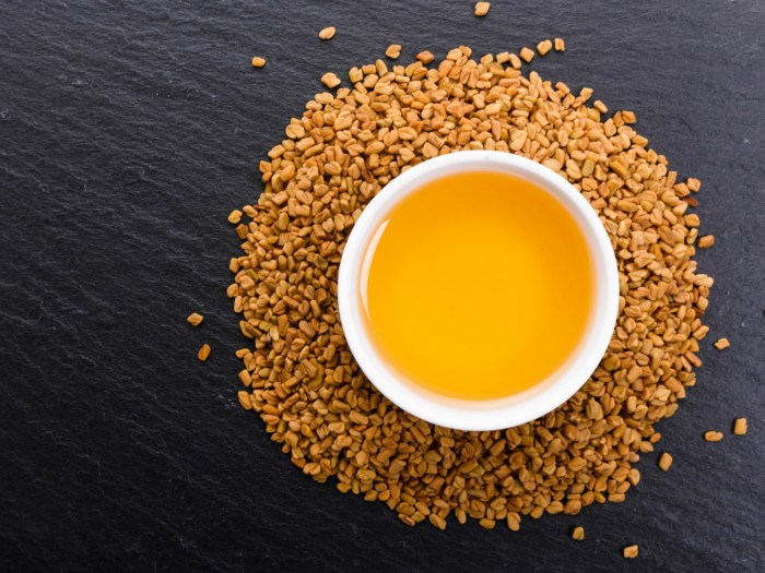 Fenugreek seeds around a bowl with fenugreek oil on a dark counter