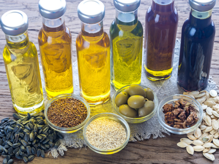 Different varieties of oil next to bowls of sunflower seeds, olives, sesame seeds