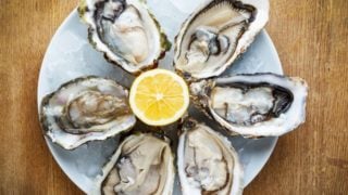 Fresh oysters served with ice and lemon on a white plate and kept on a wooden table