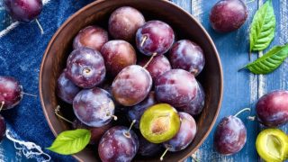 A basket with ripe plums with leaves on the blue table