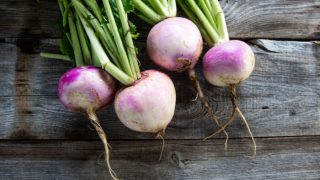 Close-up image of turnips with fresh green roots on a wooden background