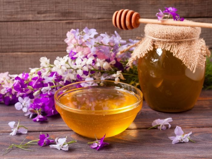 Un barattolo e una ciotola di miele millefiori con fiori freschi bianchi e viola su un tavolo di legno